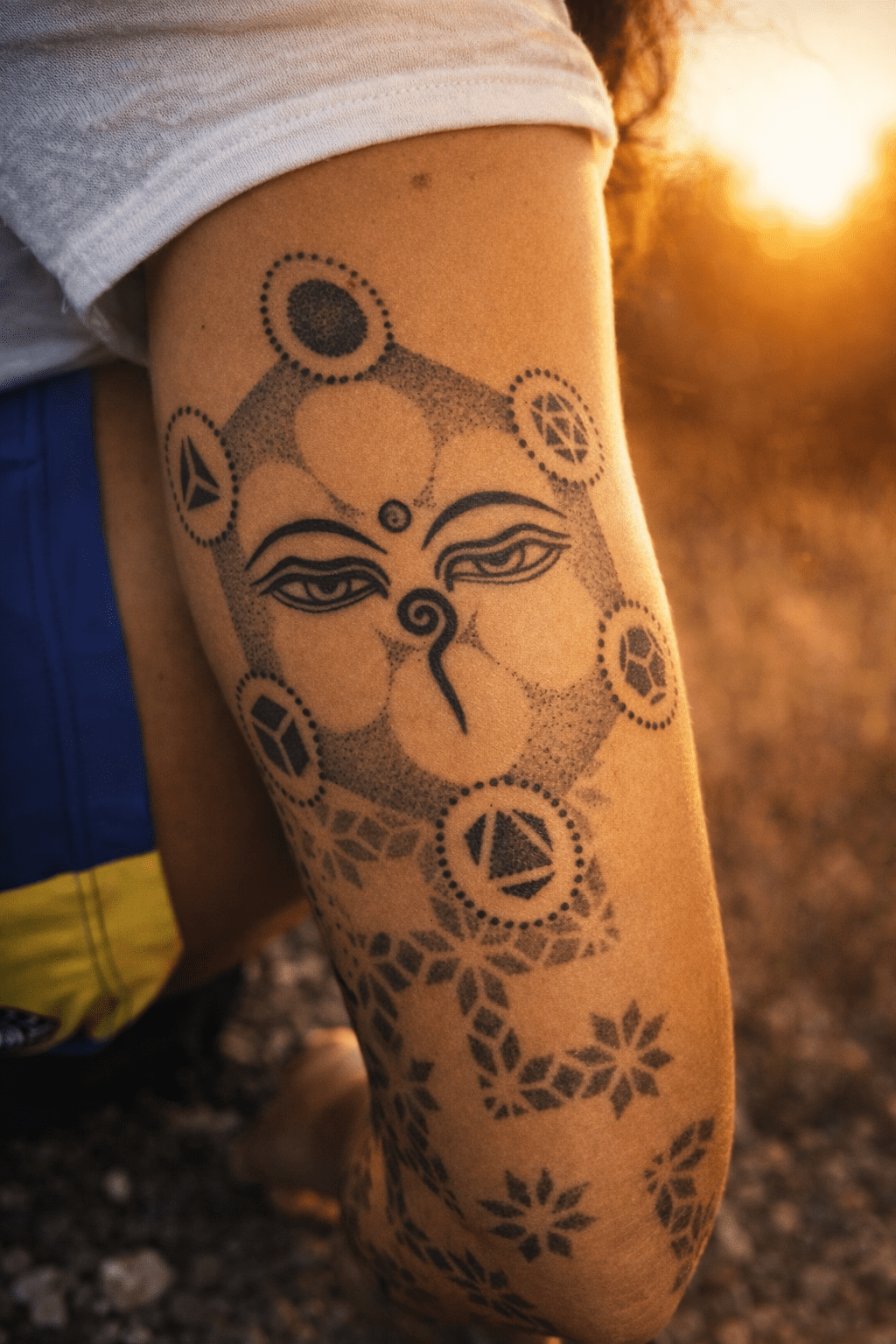 Tatuaje de ojos de Buda en bíceps con geometría de sólidos platónicos, diseño simbólico artístico realizado en Gran Canaria.